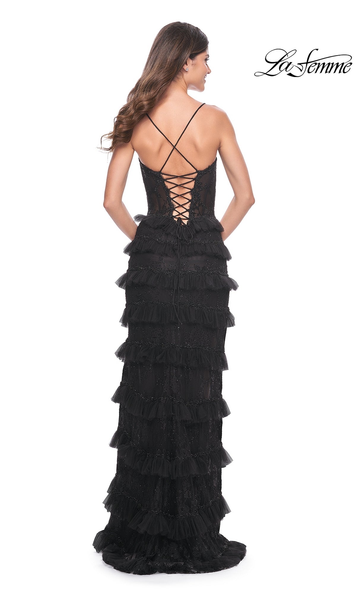 A woman models the La Femme Long Black Ruffled Prom Dress 32113 with thin straps and a lace-up back, standing against a white background. The